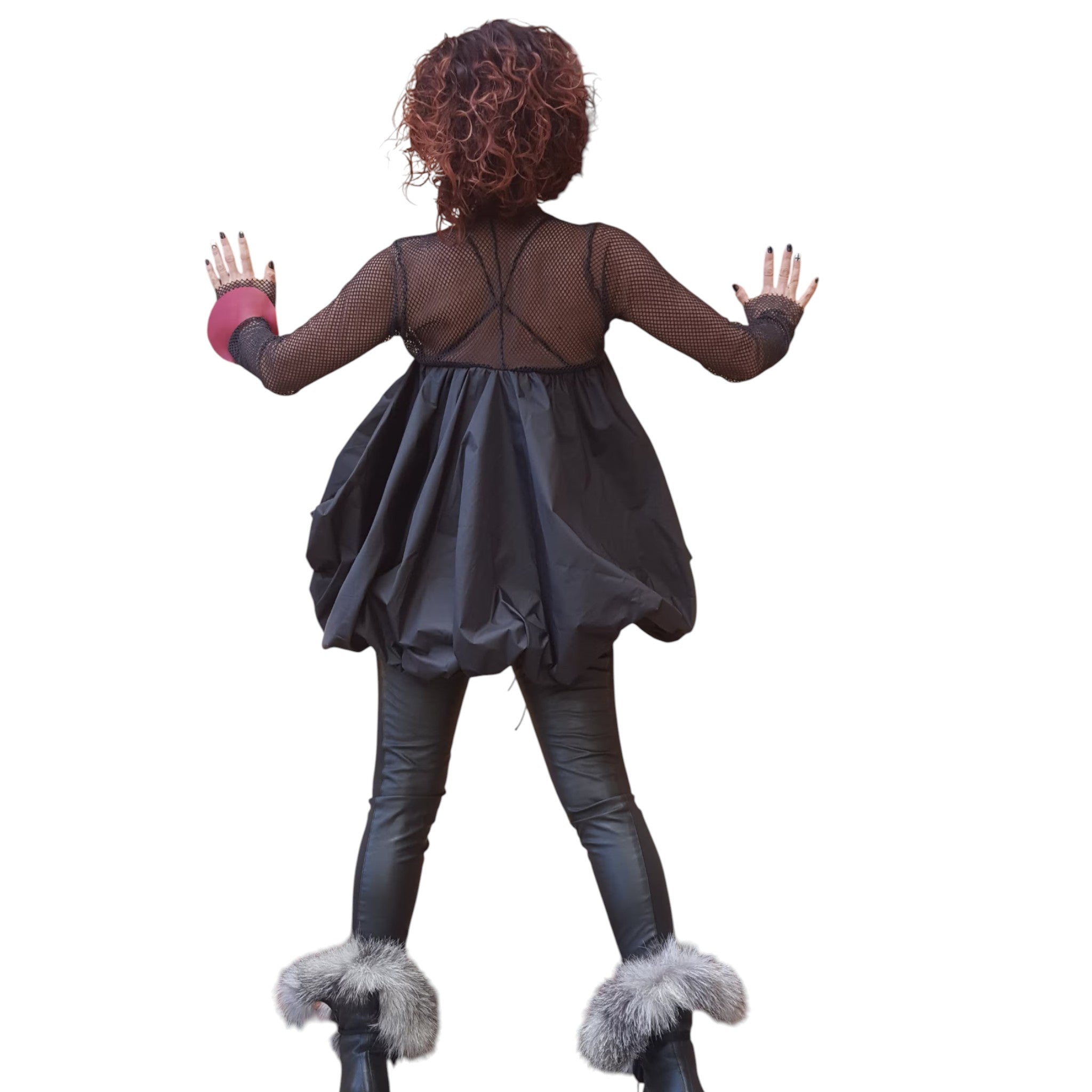 A woman with curly hair wearing a black dress and fur boots stands with her arms outstretched.