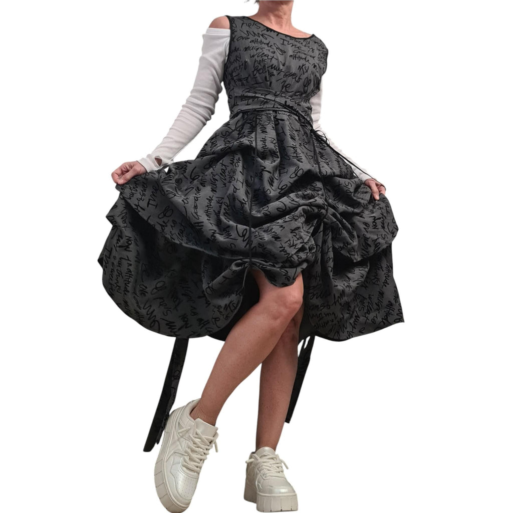May include: A dark gray dress with a black script pattern, featuring a unique gathered skirt design. The dress has a fitted bodice and a cinched waist, paired with a white long-sleeved top. The outfit is completed with white platform sneakers.