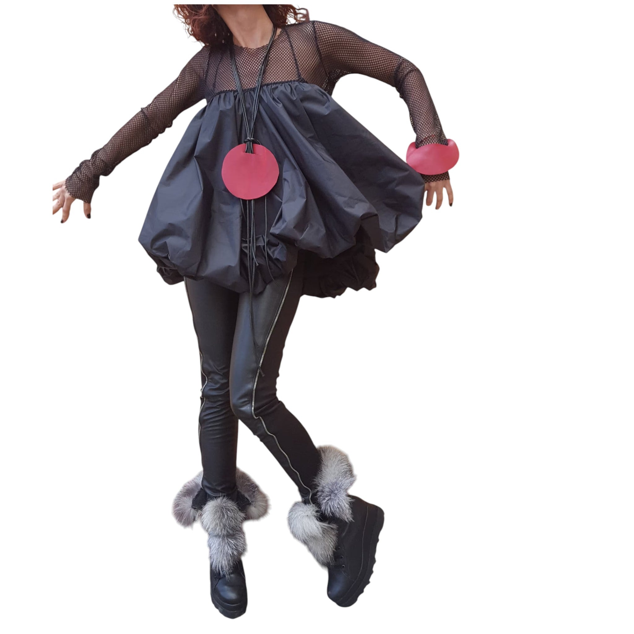 A woman wearing a black dress with a large, puffy skirt, black leggings, and black boots with fur trim, posing with her arms outstretched.