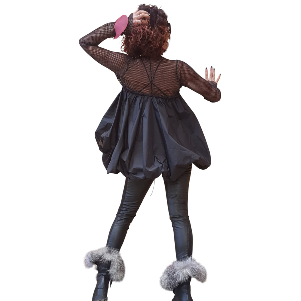 A woman with curly hair is standing with her back to the camera, wearing a black dress and fur boots.