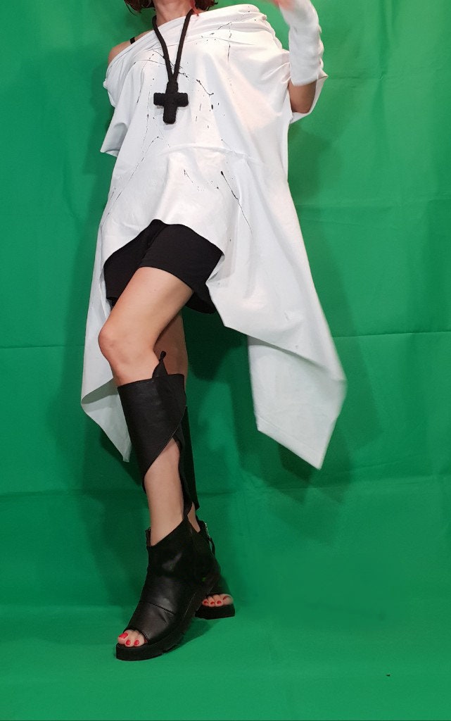 May include: A white, asymmetrical, oversized t-shirt with black paint splatters. The t-shirt is paired with black shorts and black open-toe heeled sandals.